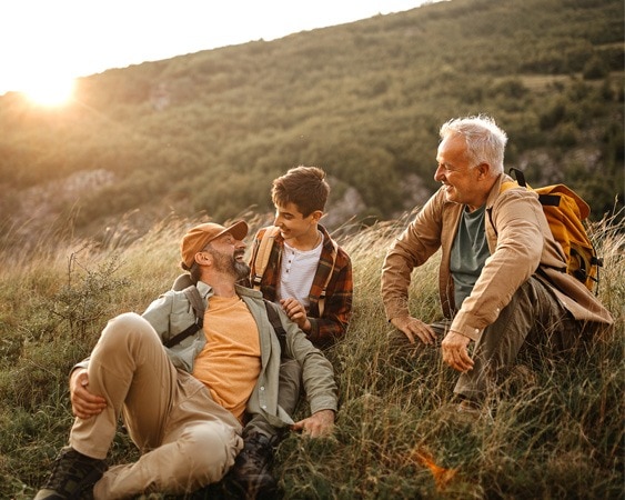 Drei Generationen von Männern genießen eine Wanderpause im Sonnenuntergang