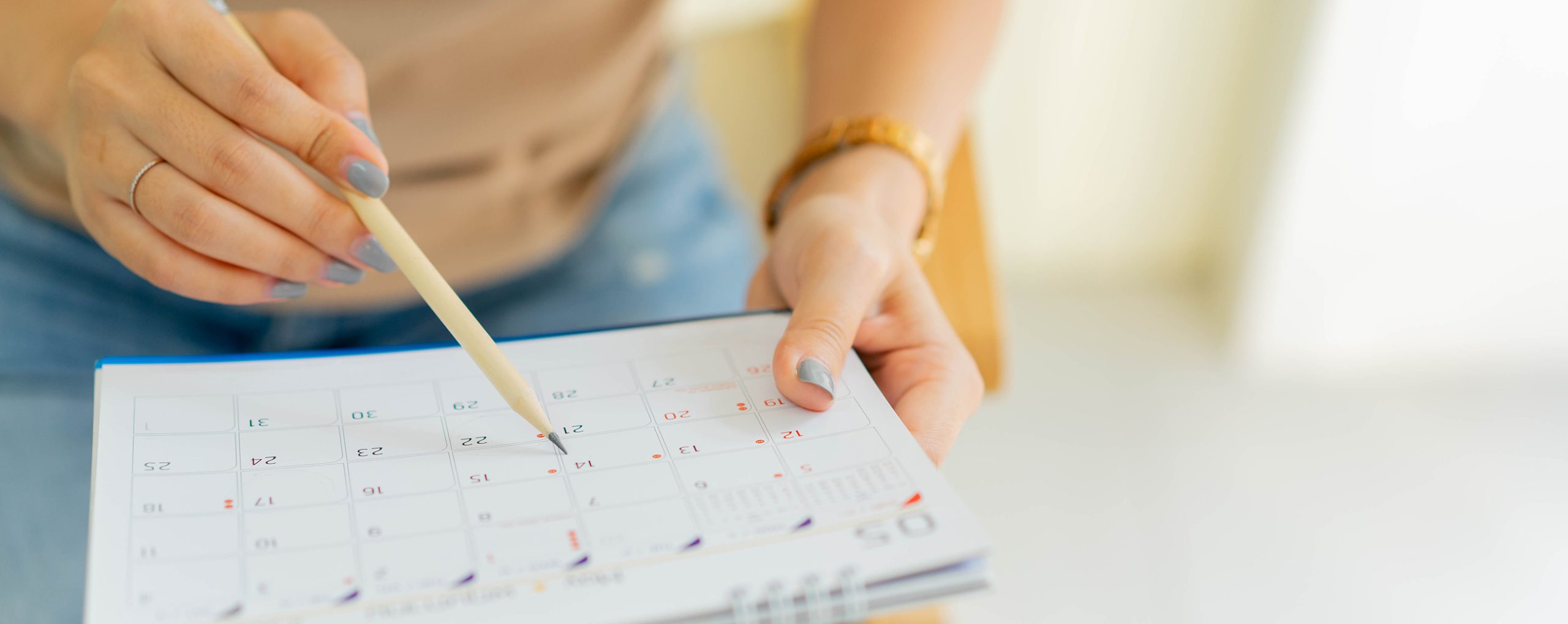 Hände mit Kalender und Bleistift für Terminplanung.