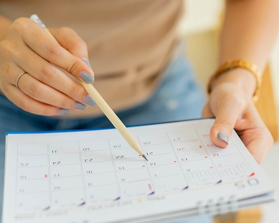 Hände mit Kalender und Bleistift für Terminplanung.