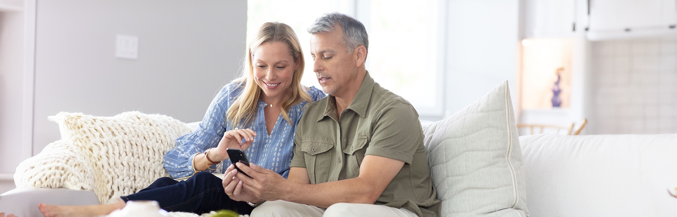Paar sitzt auf einem Sofa und schaut gemeinsam auf ein Smartphone.