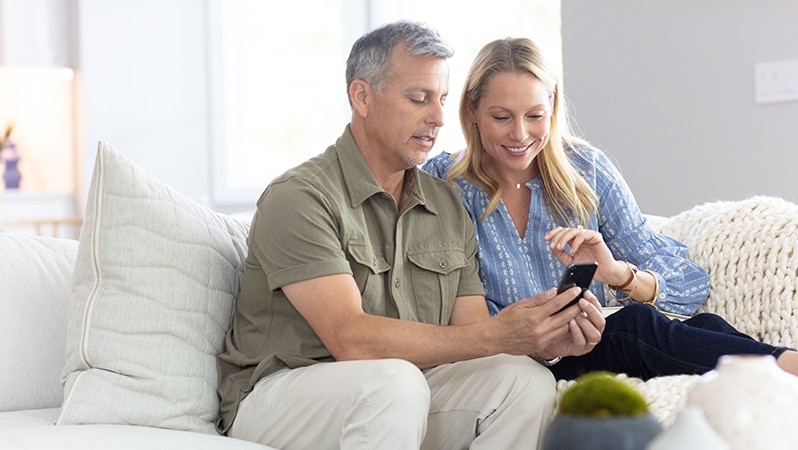 Paar sitzt auf einem Sofa und schaut gemeinsam auf ein Smartphone.