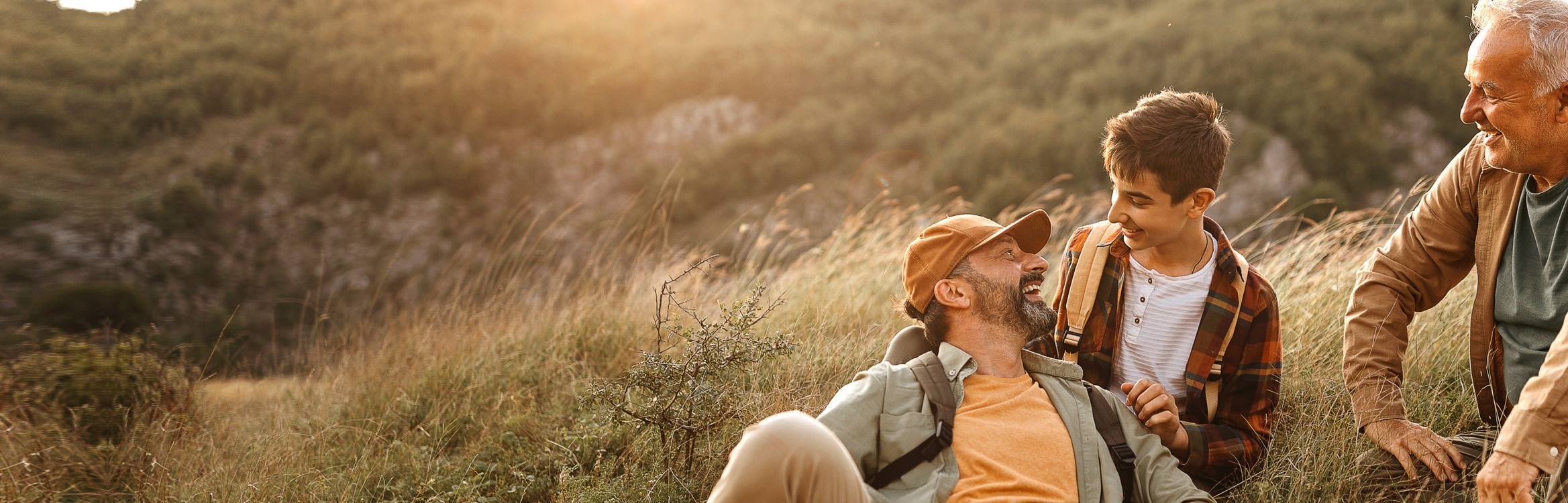 Drei Generationen Männer sitzen lachend beim Wandern.