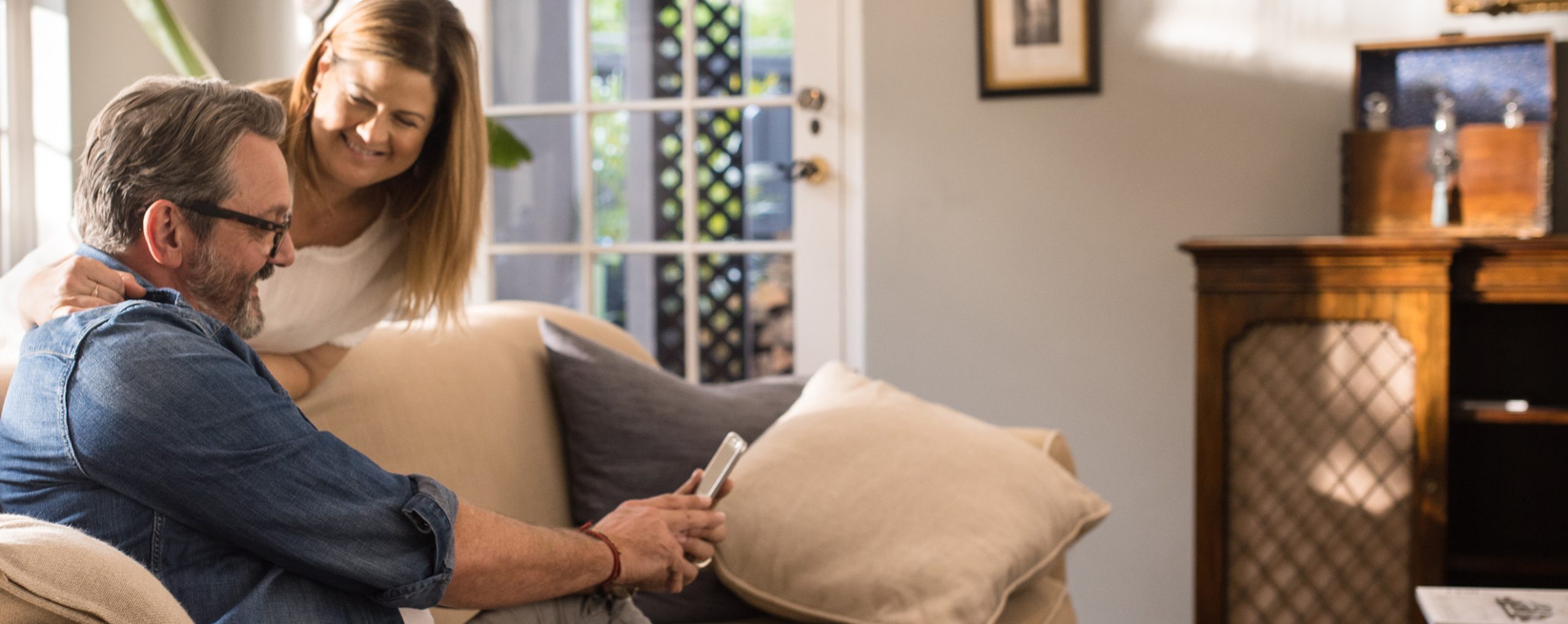 Ein älteres Paar sitzt auf einem Sofa und schaut gemeinsam auf ein Smartphone.
