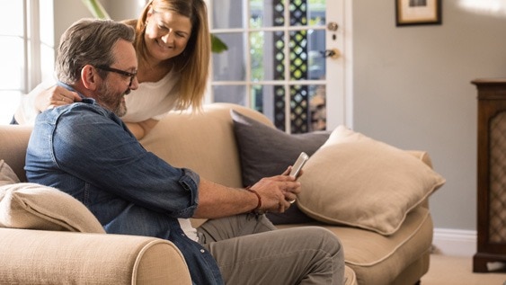 Ein älteres Paar sitzt auf einem Sofa und schaut gemeinsam auf ein Smartphone.