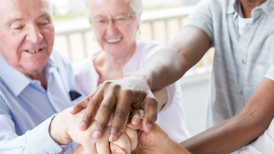 Mehrere Hände verschiedener Menschen, die übereinander liegen, symbolisieren Gemeinschaft und Unterstützung.